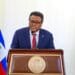Fritz Alphonse Jean au micro, devant un drapeau haïtien en berne, illustrant l’incertitude et la lourde responsabilité face à la crise nationale.